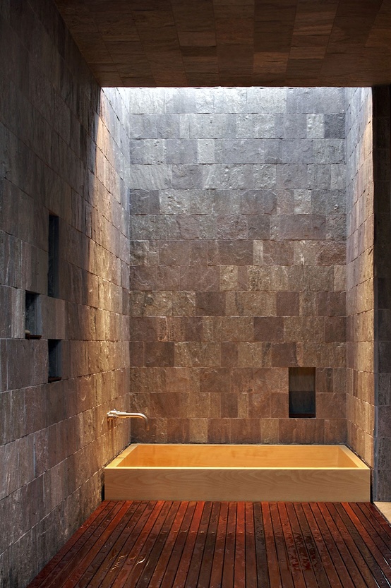 A rustic bathroom with stone walls and a wooden floor plus a built in bathtub and a skylight