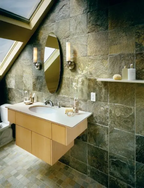 a chic attic bathroom with stone tiles on the wall and tiles on the floor plus a large attic window