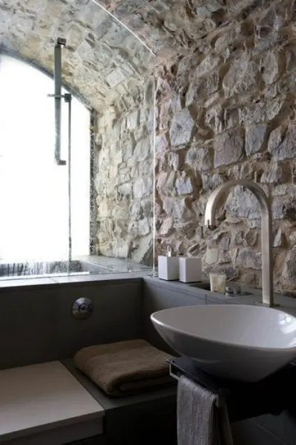 A contemporary bathroom with rough stone walls and a ceiling plus ultra modern appliances