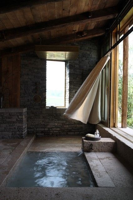 An outdoor indoor bathroom with stone walls and a floor plus a built in bathtub