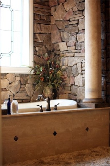 Natural stone walls and a bathtub clad with light colored wood plus a pillar for a chic eclectic look