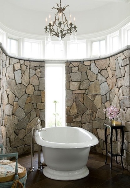 a gorgeous bathroom clad with stone, with a chic crystal chandelier, refined furniture and blooms