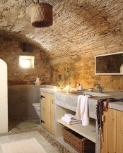 a wabi-sabi bathroom with stone walls, concrete and wood furniture and a wicker lampshade