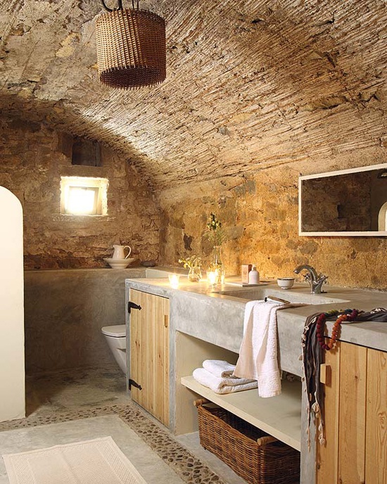 A wabi sabi bathroom with stone walls, concrete and wood furniture and a wicker lampshade