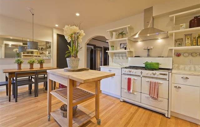 A modern white kitchen with neutral countertops and open shelves, a light stained kitchen island that can be folded