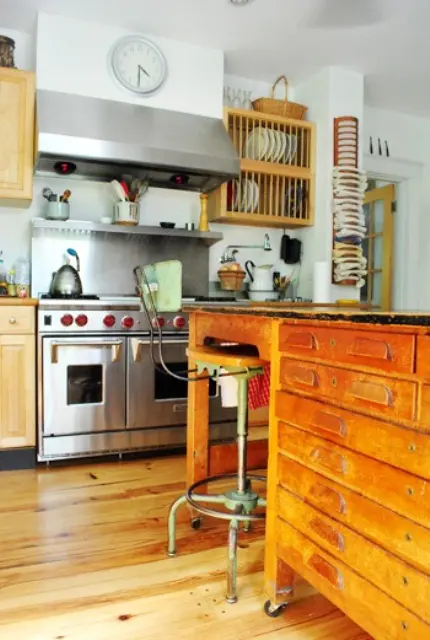 A light stained kitchen with stainless steel appliances and a kitchen island made of a vintage industrial desk for a unique look