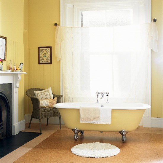 A cozy vintage sunny yellow bathroom with a non working fireplace, a clawfoot bathtub, a curtain, artwork and a woven chair is very welcoming