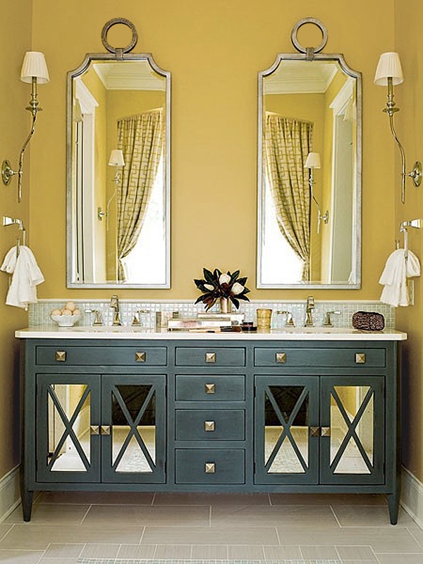 A chic bathroom with mustard walls, a navy double vanity, mirrors in eye catchy frames and neutral textiles and sconces