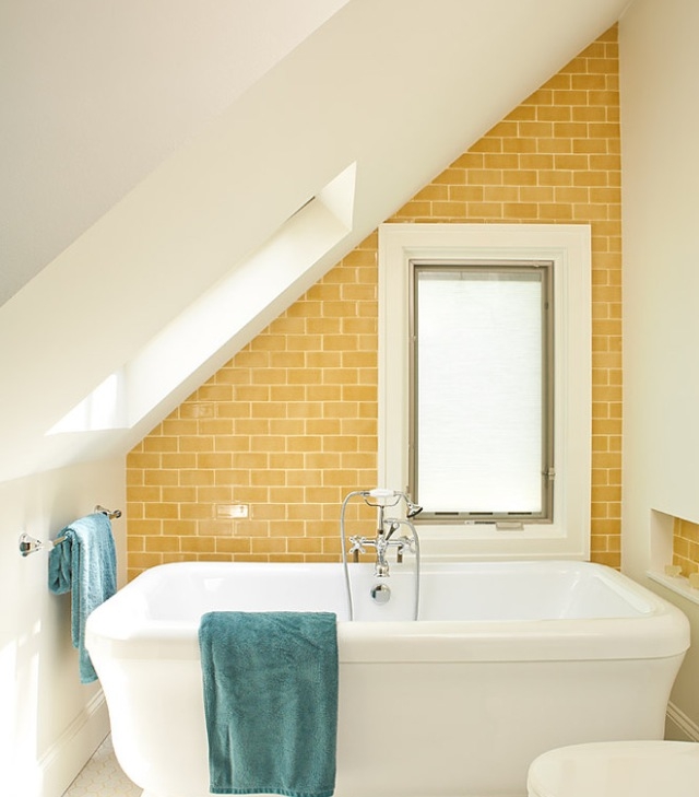 a small and lovely attic bathroom with a skylight, a yellow tile accent wall, a square bathtub and a small window with frosted glass
