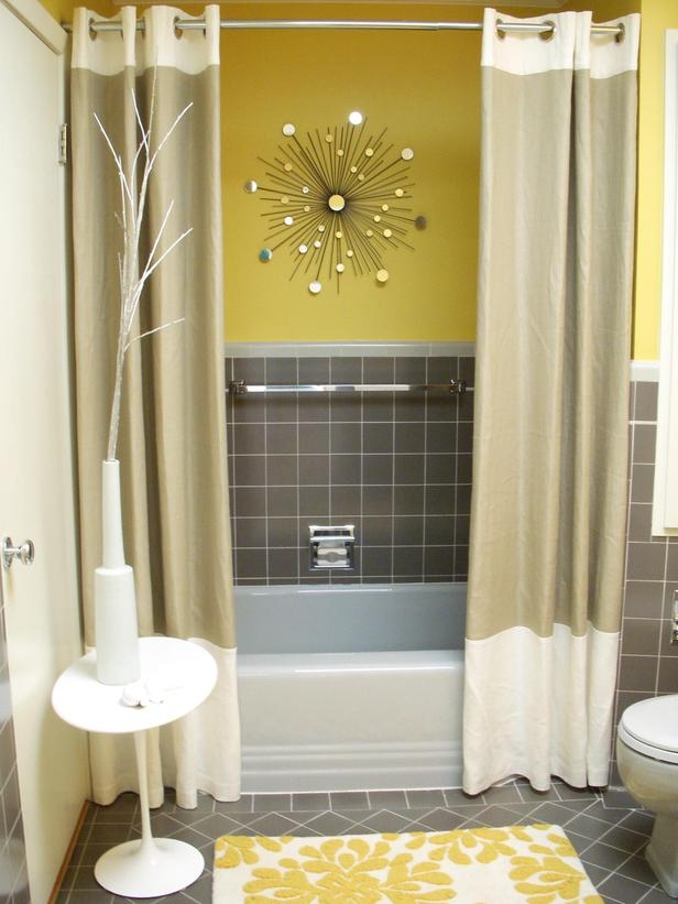 An eye catchy bathroom with yellow and grey decor, with taupe tiles and yellow walls, matching curtains and a yellow printed rug