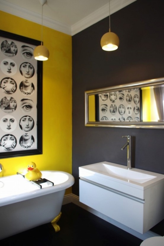 a bold modern bathroom with a bright yellow wall and a gray one, an eye-catchy artwork and white appliances and a long and narrow mirror