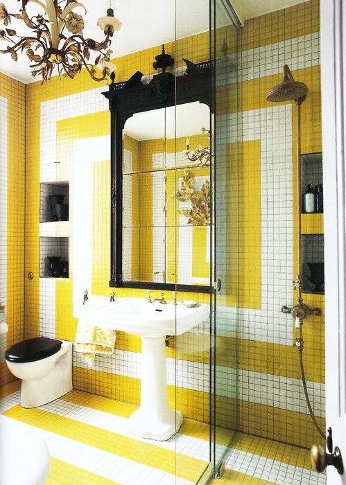 A bold bathroom clad with yellow and white tiles with geometric patterns, a mirror in a window frame, some other black touches for an eye catchy look